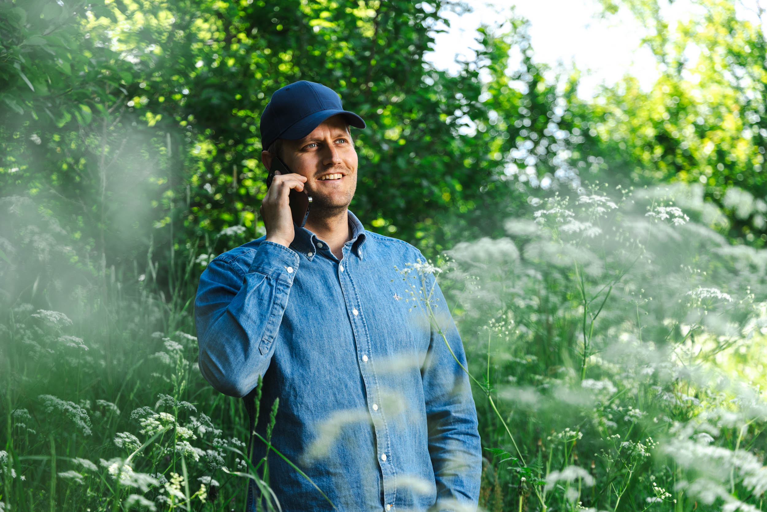 Thomas, kundeutvikler i Akari, står i en blomstereng mens han snakker i telefonen