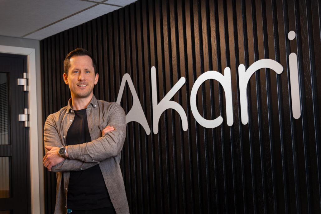 Geir i Akari står med armene i kors foran en stor Akari-logo på veggen, i kontoret på Kongsberg