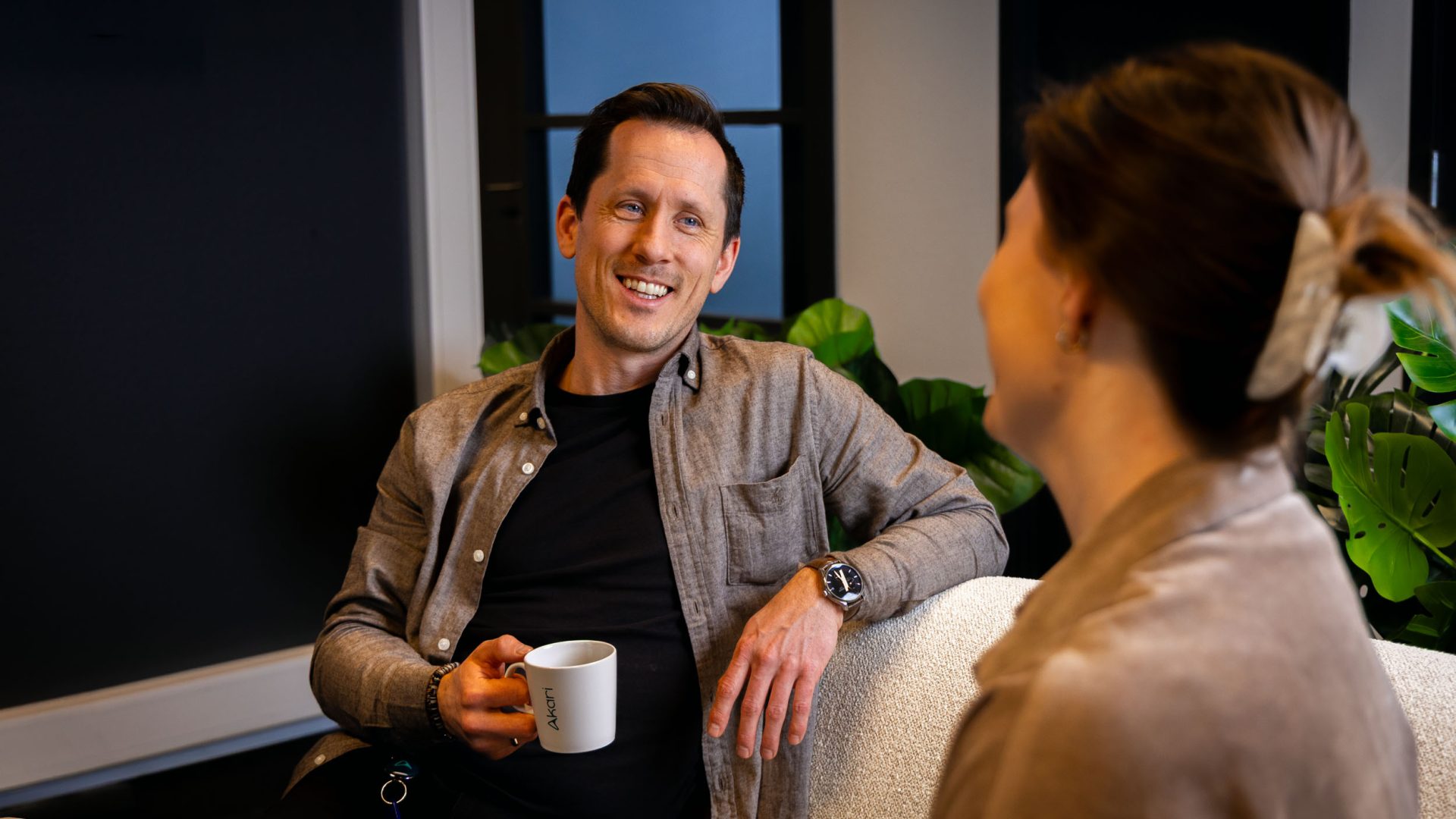 Geir smiler mot sin kollega Pia mens han holder en kaffekopp i hånden